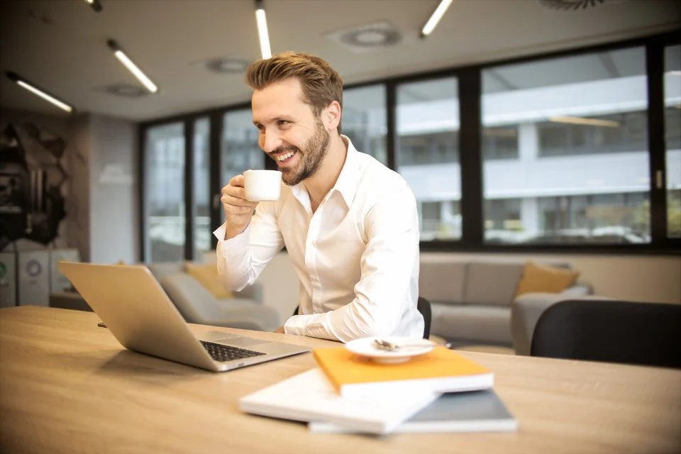 Smiling man with coffee at a bright office desk