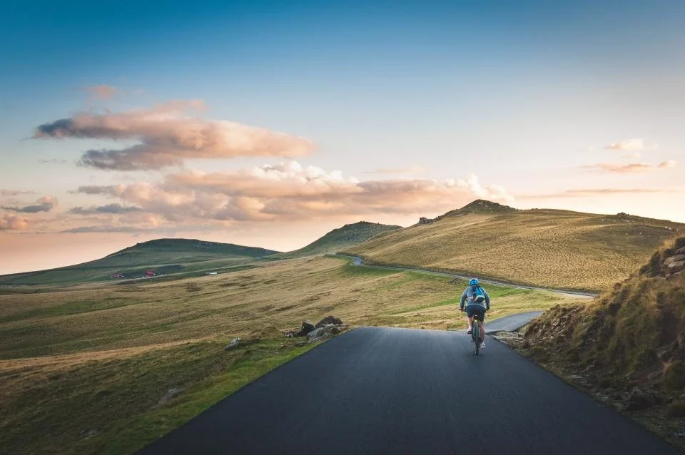 Cyclist riding a country road through green hills