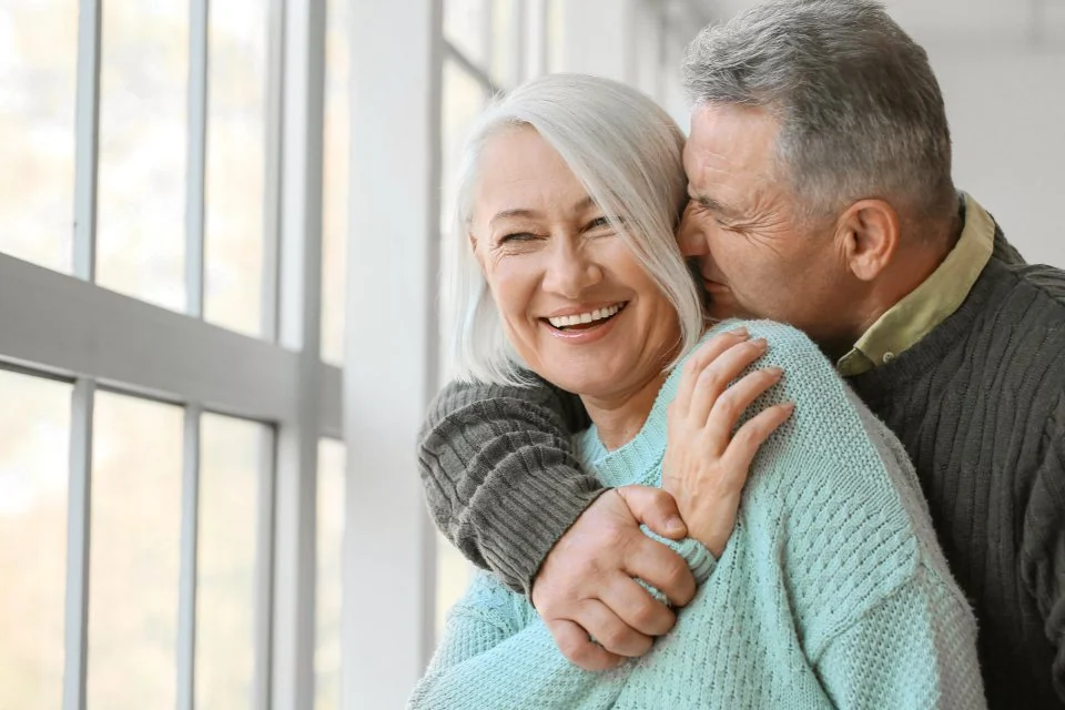 Mature couple embracing and smiling by a sunny window