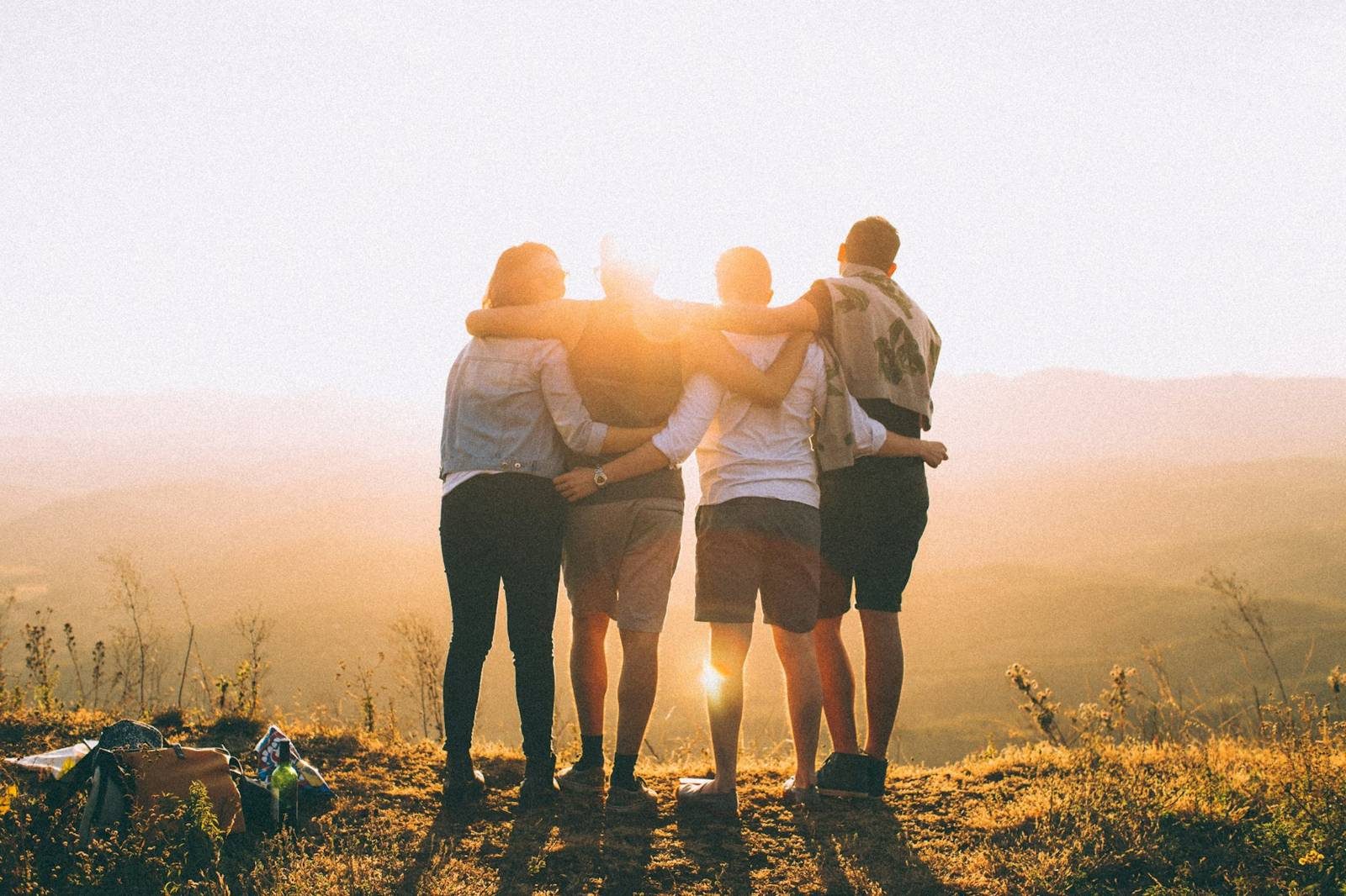 Four friends with arms around each other watching the sunset outdoors