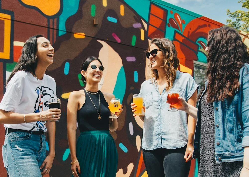 Group of women laughing together in front of a colorful mural